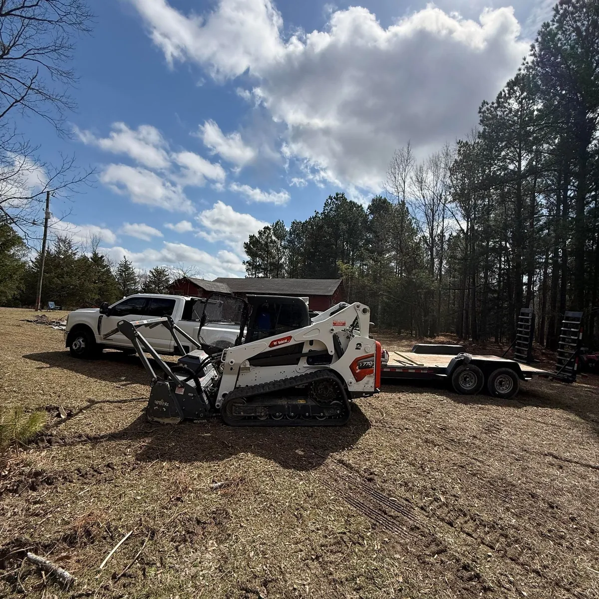 BrushKat’s forestry mulcher beside open ground and an equipment trailer